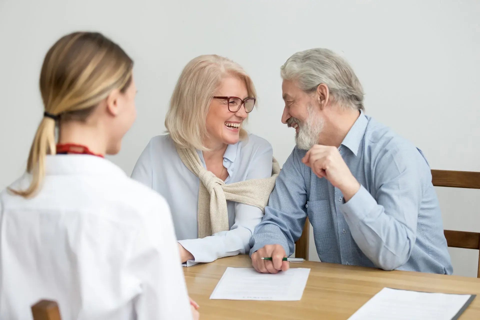 Senior couple meeting advisor at desk, reviewing documents and smiling during financial consultation.